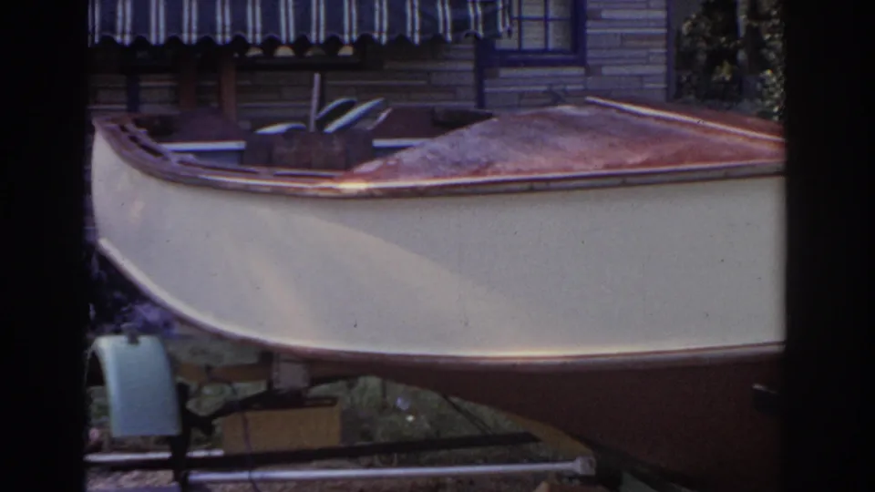 The 8mm frame shows the side of a small boat on a trailer beside the house and shaded yard area.