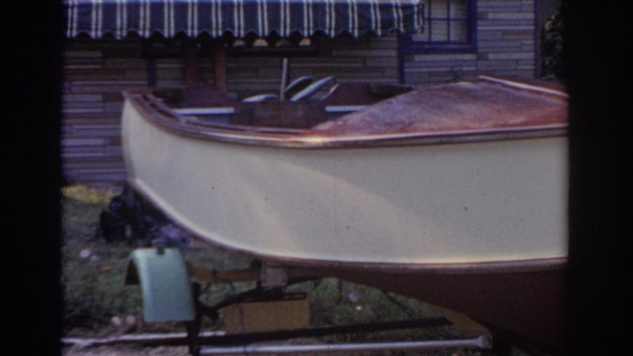1963 New Jersey 8mm frame showing a small cream boat on a trailer in a grassy backyard near a house with a striped awning.
