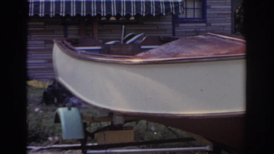 1963 New Jersey 8mm frame showing a small cream boat on a trailer in a grassy backyard near a house with a striped awning.