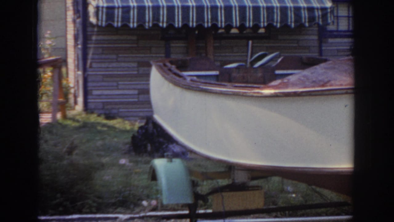 Boat bow and trailer in a grassy yard near house siding and an awning.