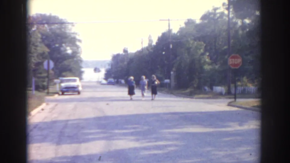 1963 New Jersey street scene showing three women walking near a stop sign, with a period car and tree-lined road in view.