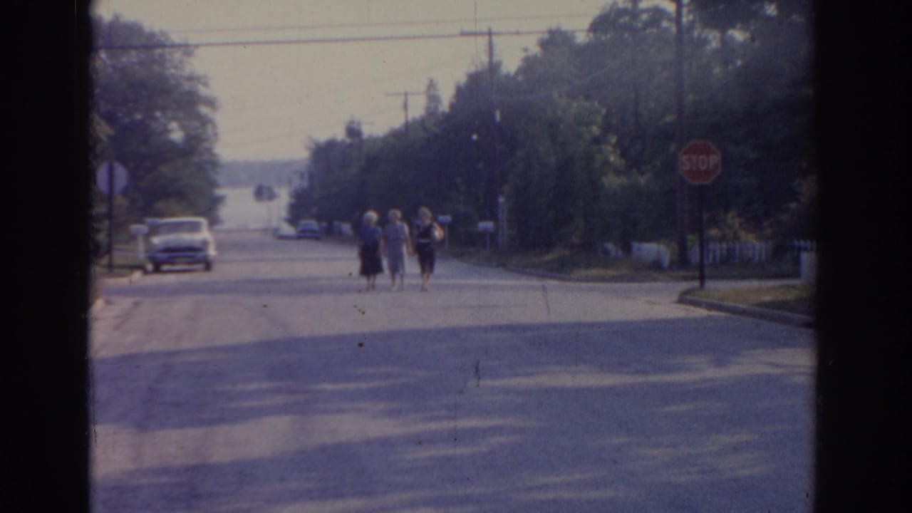 Three women walk closer on a wide street with a stop sign at the corner.