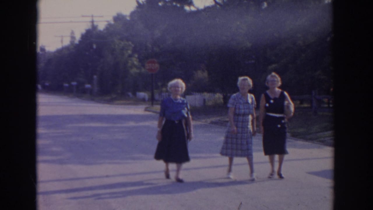 Three older women walk side by side on a sunlit New Jersey residential street in 1963 home-movie footage.