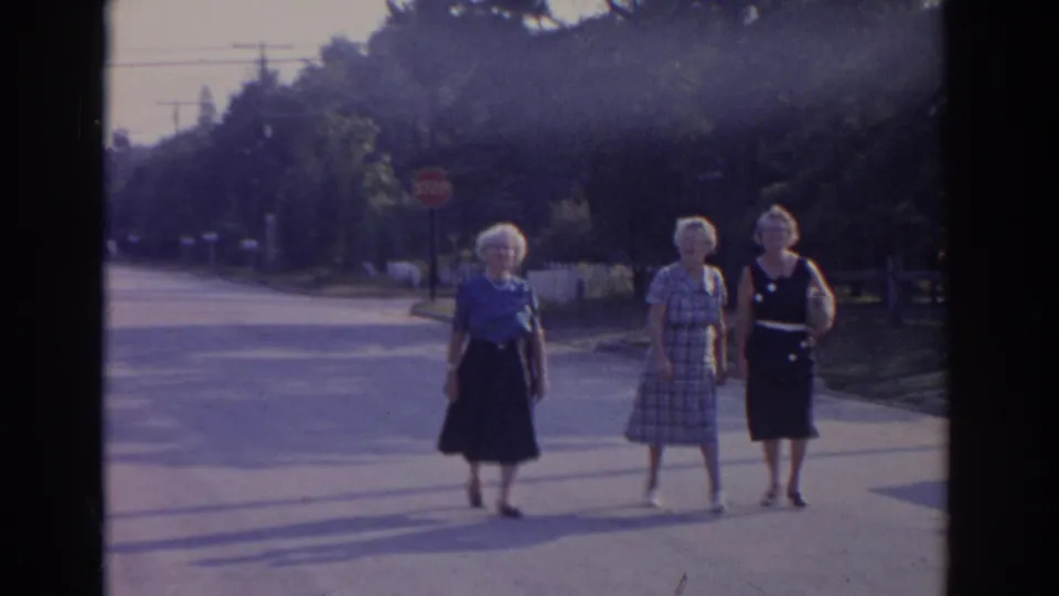 Three older women walk side by side on a sunlit New Jersey residential street in 1963 home-movie footage.
