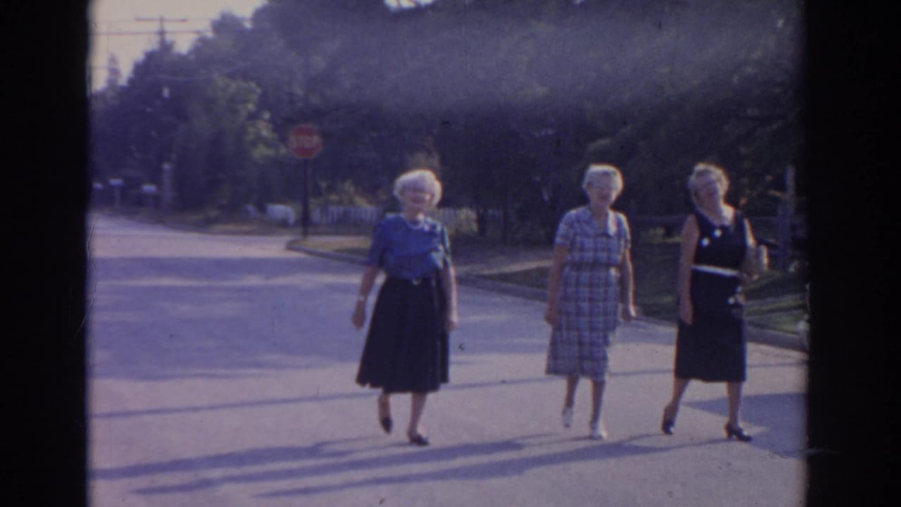 Three older women continue walking across a bright suburban street.