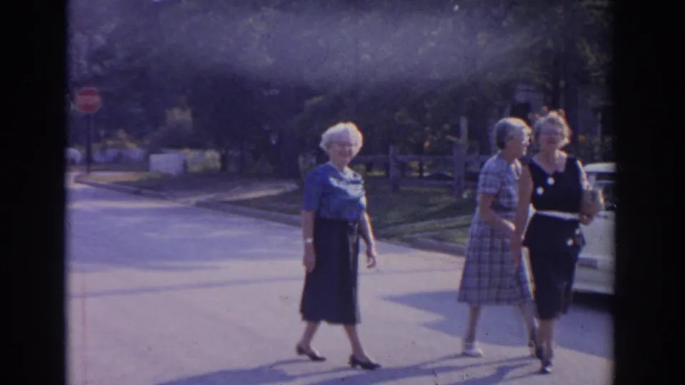 Three older women continue past the camera on a tree-lined New Jersey street, seen in soft 8mm color.