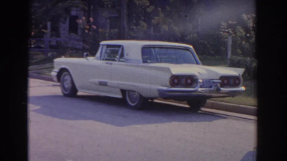 1963 New Jersey home-movie frame focused on a white classic car parked along a quiet residential street.