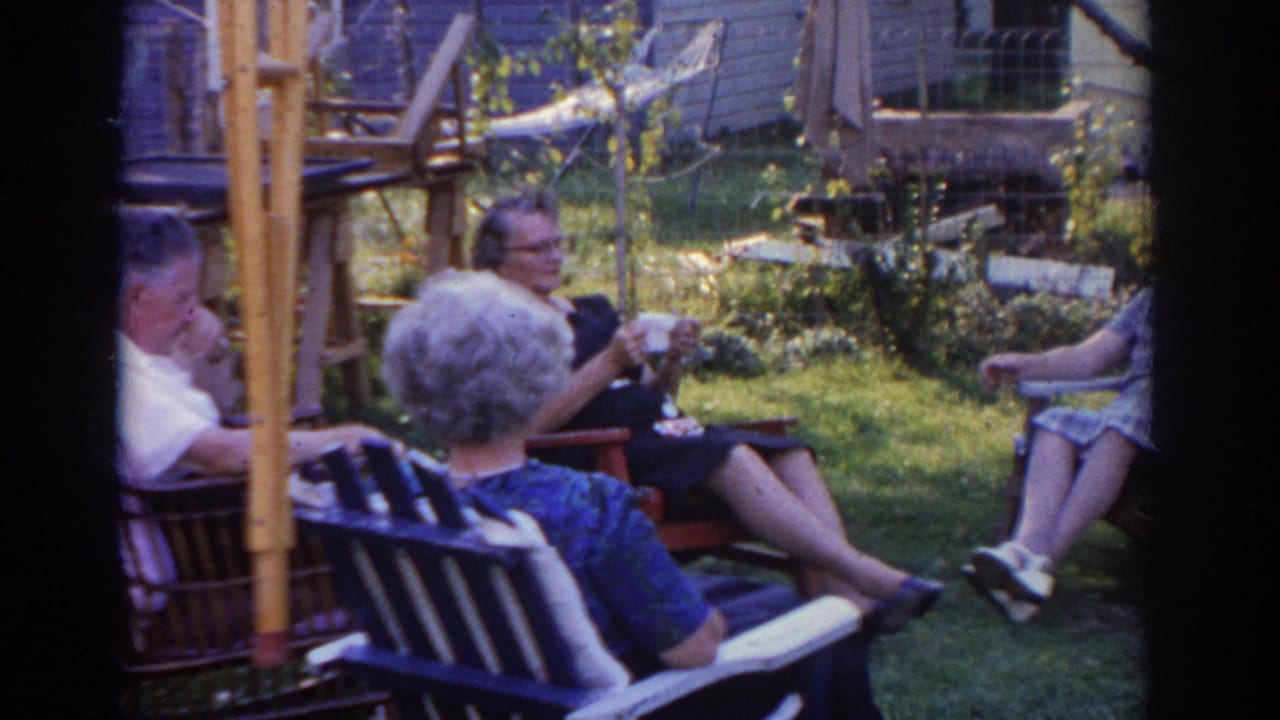 Older adults sit in chairs while one person holds a cup or napkin.