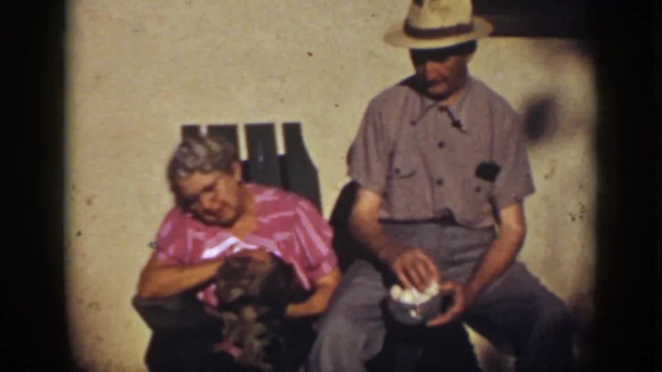 In Auburn, California home-movie footage from 1939, an elderly woman holds a small cat while an elderly man sits beside her with a bowl of eggs.