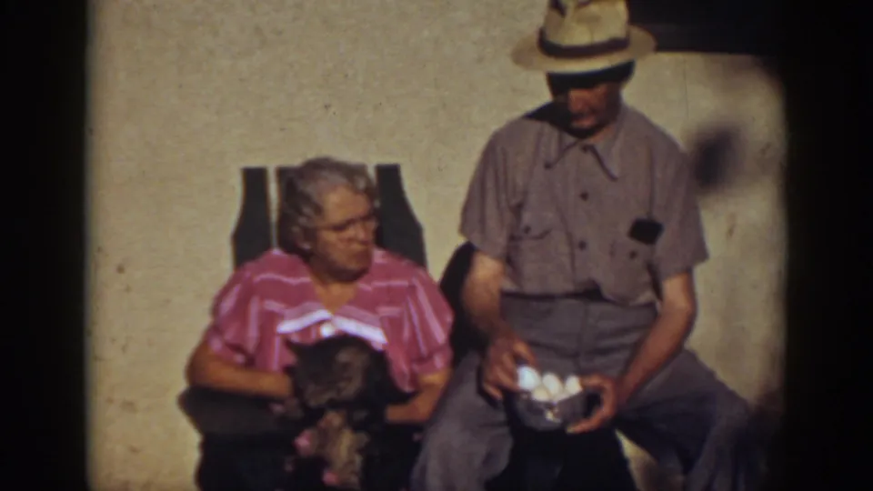 A seated elderly couple in Auburn, California, with the woman holding a small cat and the man holding a bowl filled with eggs.