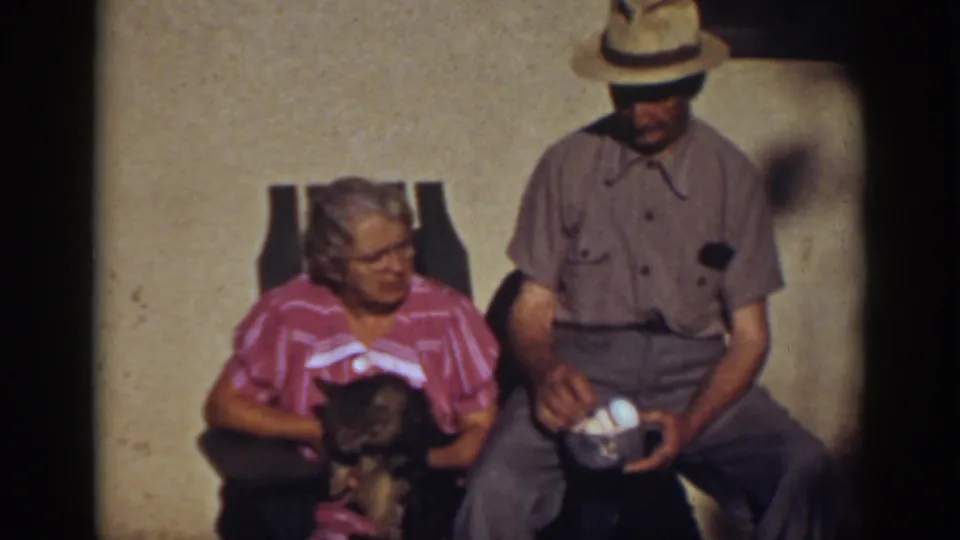 At the end of the clip, the older couple sit close together outdoors, the cat visible near the woman and eggs visible in the man's bowl.
