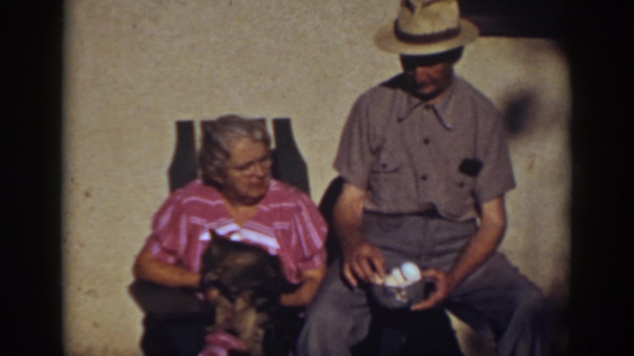 In 1939 Auburn, California home-movie footage, an elderly woman pets a dark cat while a seated man in a straw hat holds a bowl of eggs.