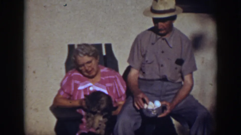 In supported 1939 Auburn, California footage, a seated woman holds a small dog beside a man in a straw hat holding eggs.