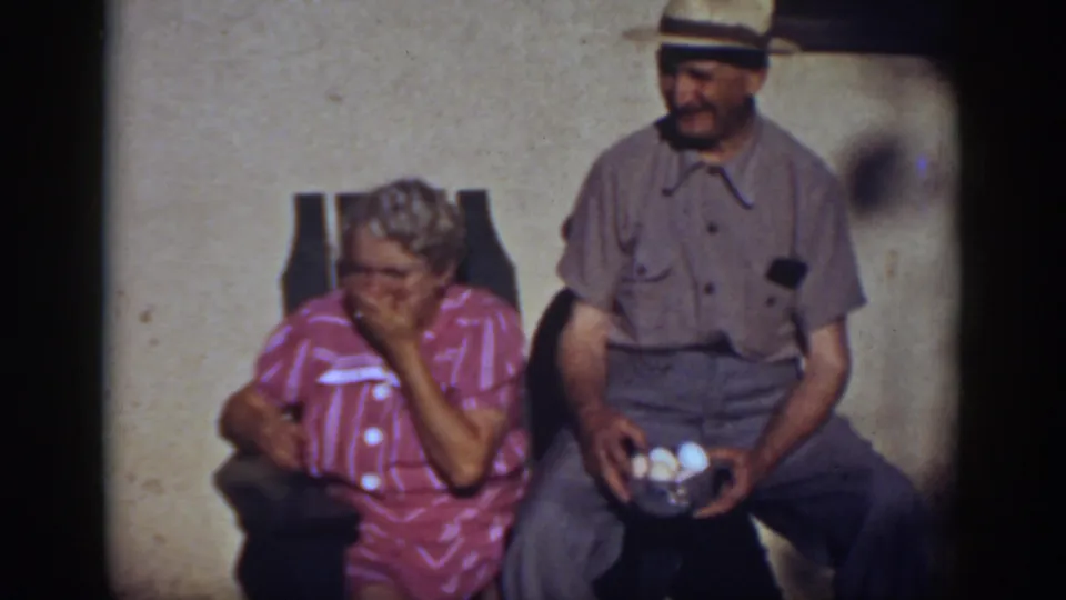 After the dog leaves the frame, the woman raises a hand to her mouth as the man remains seated with the bowl of eggs.