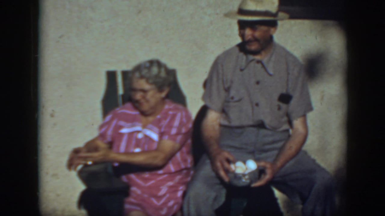 In 1939 Auburn, California footage, an older couple sits outdoors as the man in a straw hat holds eggs and the woman rests in a chair.