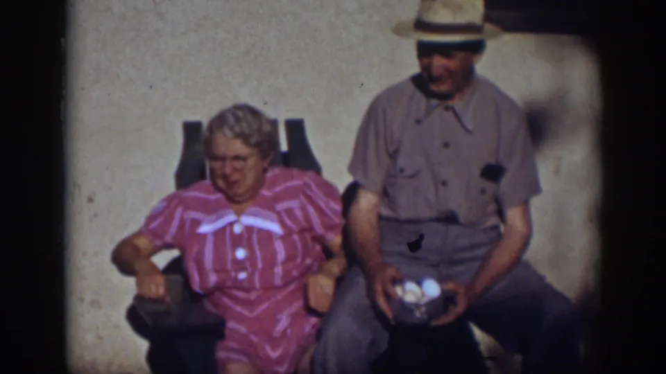 The couple sits in sunlit outdoor chairs in Auburn, California, with the woman facing forward and the man holding a bowl of eggs.