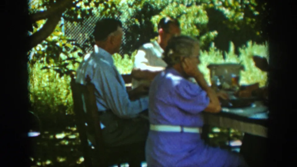 Adults seated at a shaded backyard table in Auburn, California, 1939, with plates and drink bottles visible during an outdoor meal.