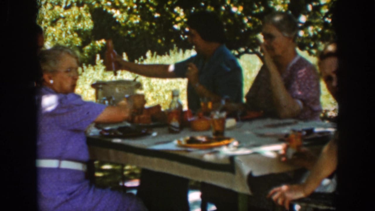 In Auburn, California in 1939, women sit at a shaded picnic table with amber glasses, plates, and serving dishes visible.