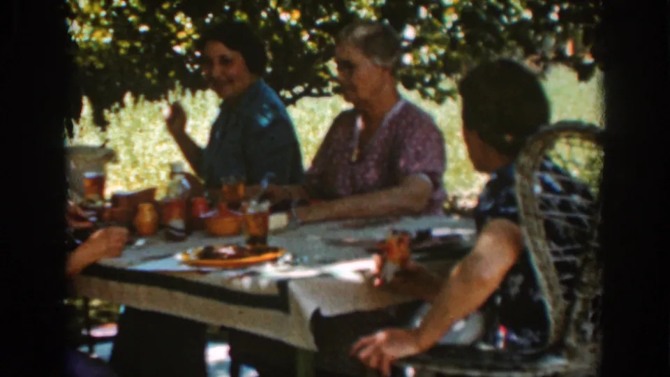 Women at an Auburn, California outdoor picnic sit in dappled shade beside plates, glasses, and a wicker chair.