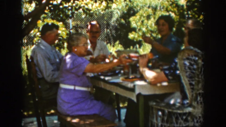 1939 Auburn home-movie frame of adults gathered at a shaded garden table with serving items and glasses.