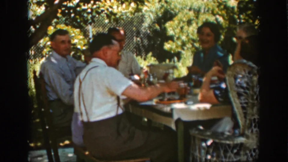 Auburn, California 1939 frame showing a man in suspenders seated with family around an outdoor lunch table beneath trees.