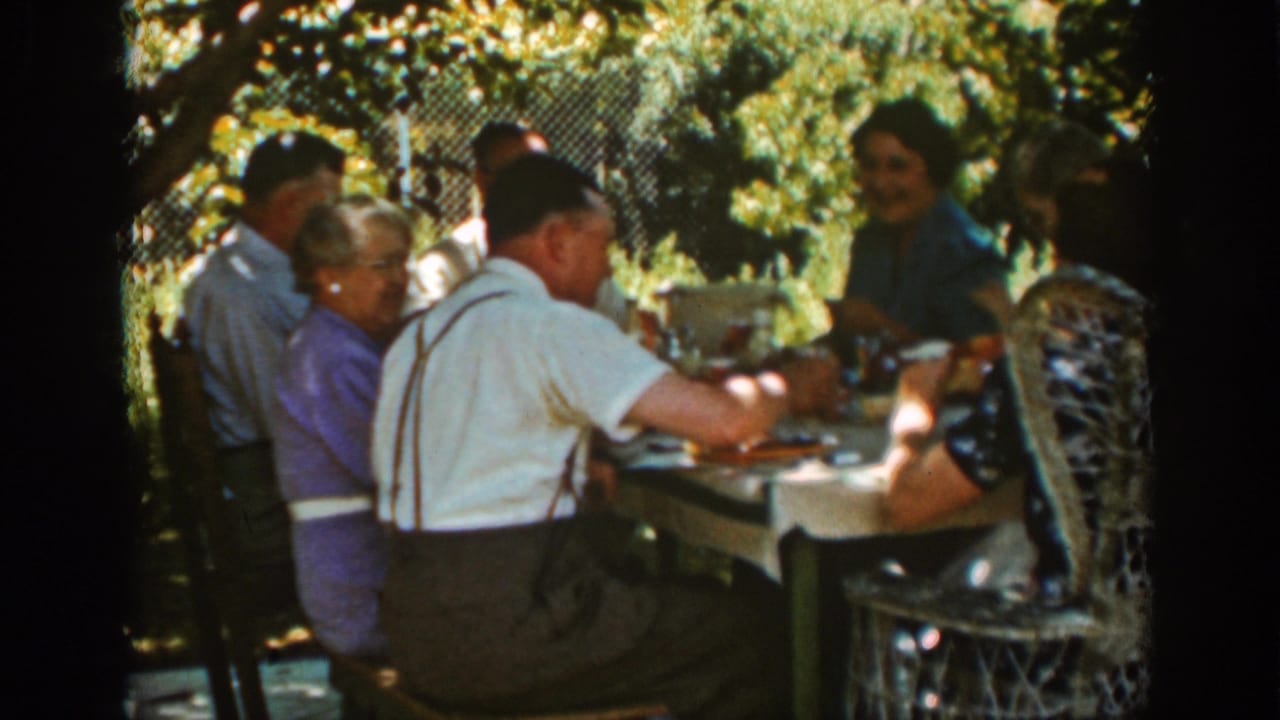 Auburn, California 1939 home-movie frame of adults gathered at a garden lunch table with foliage and a fence behind them.