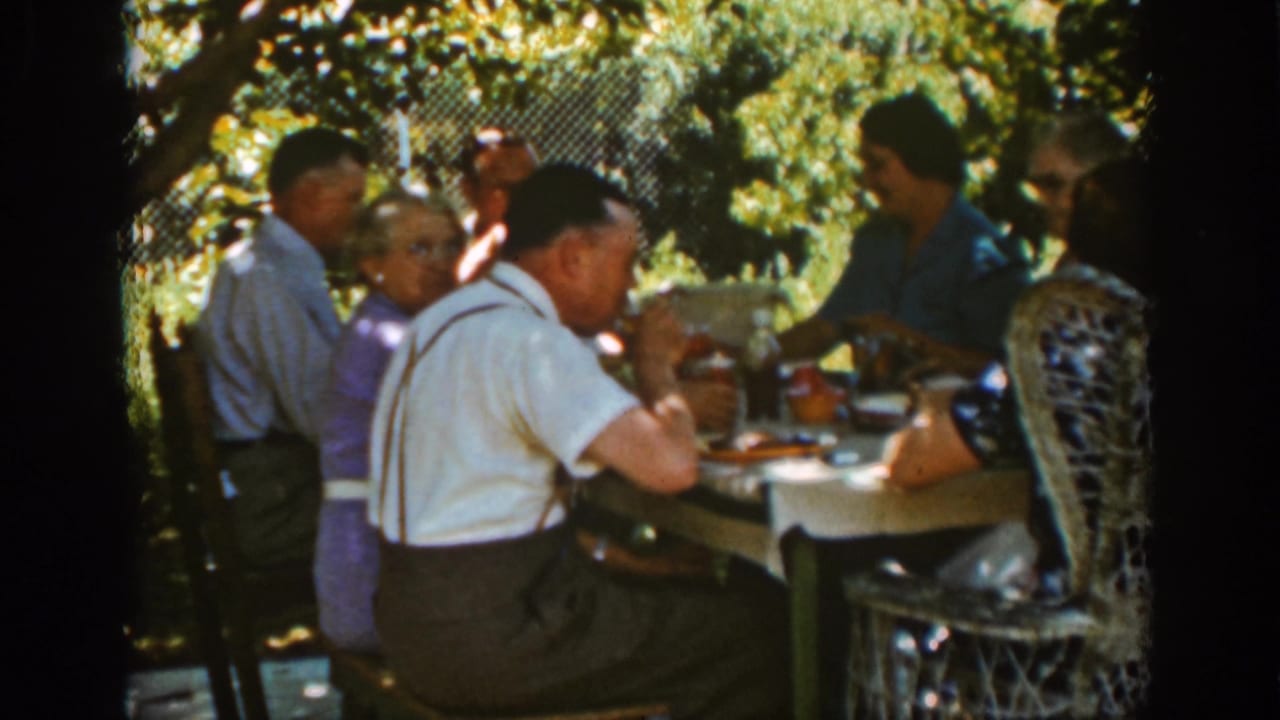 Adults continue eating at a garden table with bright foliage behind them.