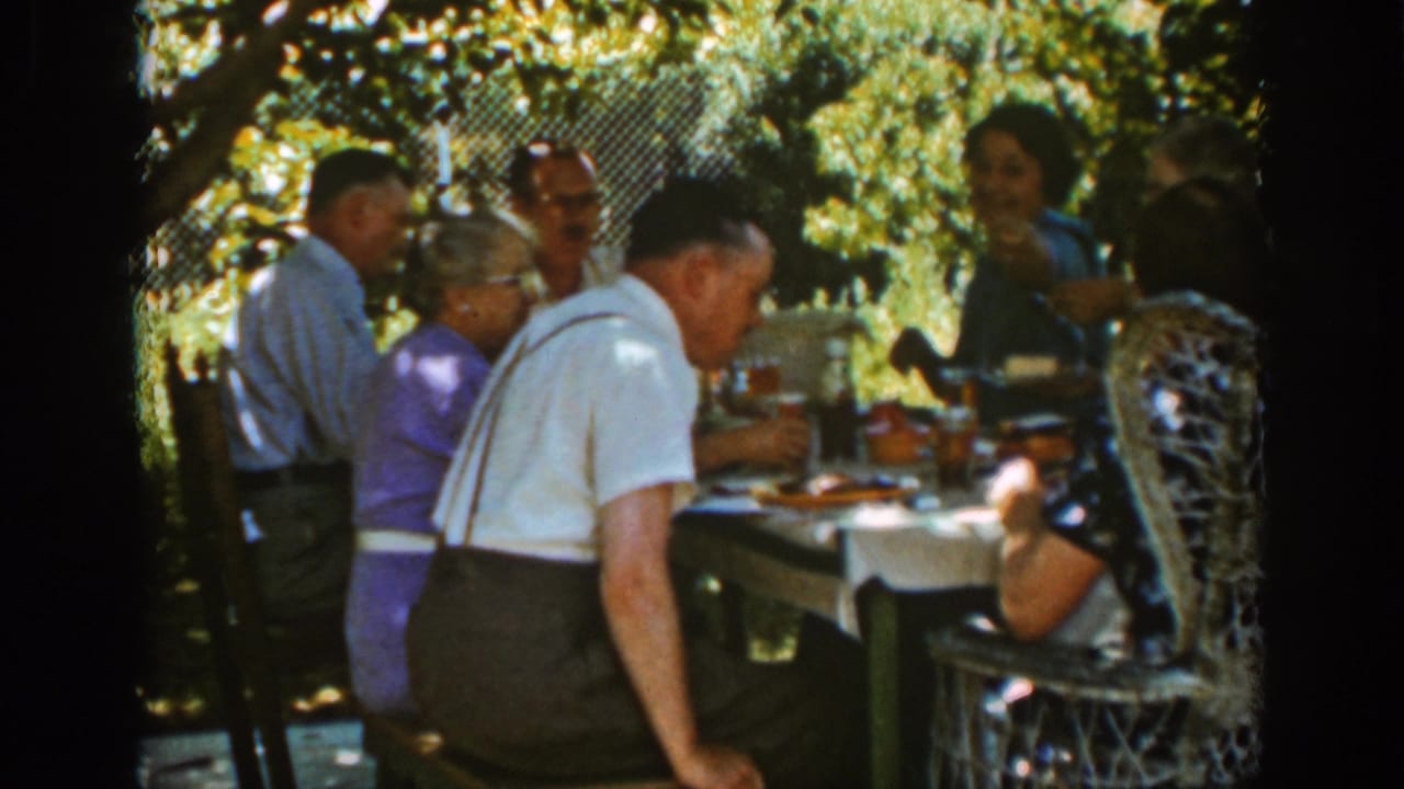 Adults seated around a shaded outdoor picnic table with food and drinks.