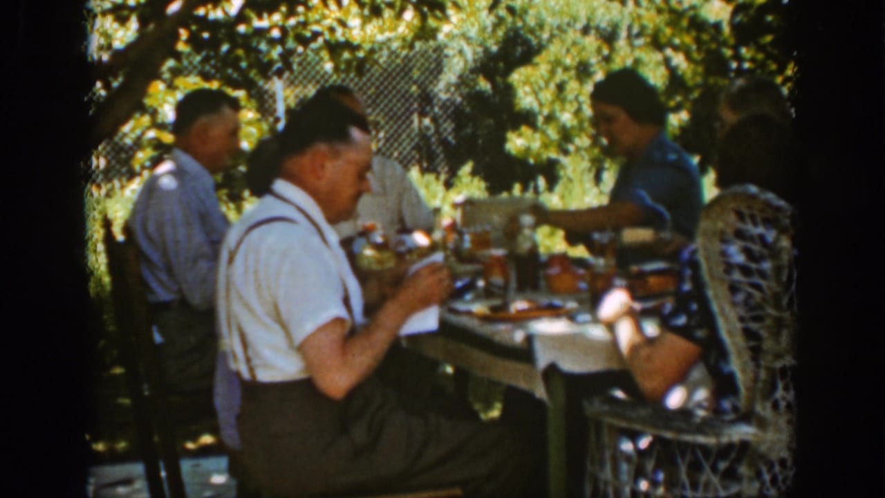 Man in white shirt and suspenders sits at a picnic table with other adults.