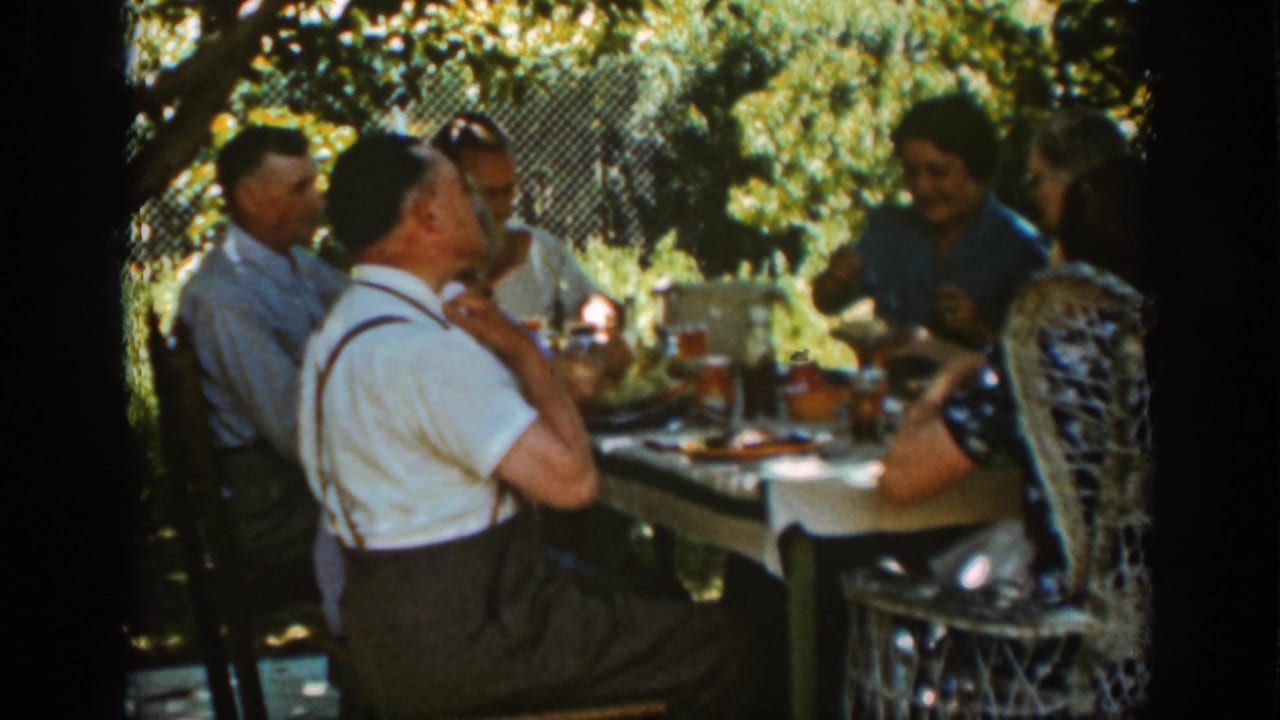 Adults seated around an outdoor picnic table under trees.