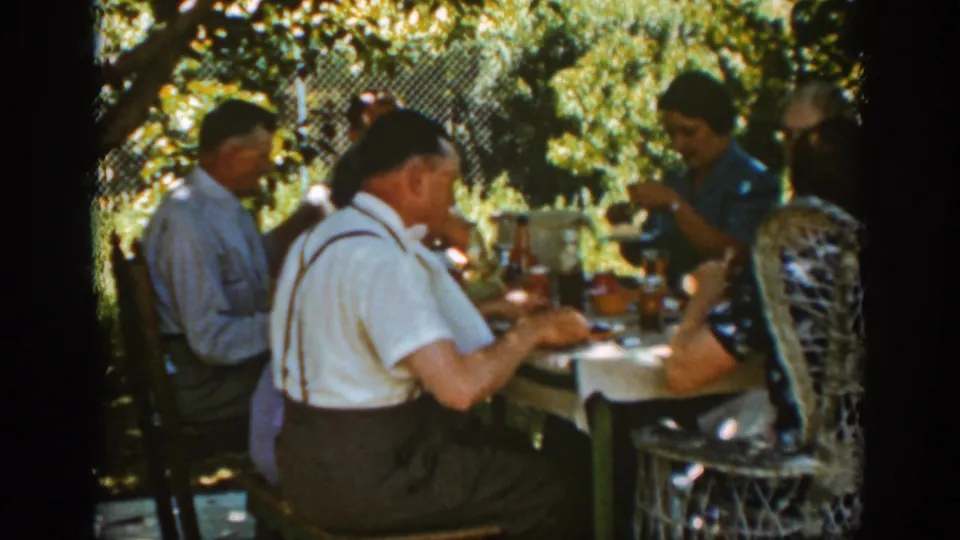 A 1939 Auburn backyard picnic scene shows adults in shirts, suspenders, and patterned dresses eating together outdoors.