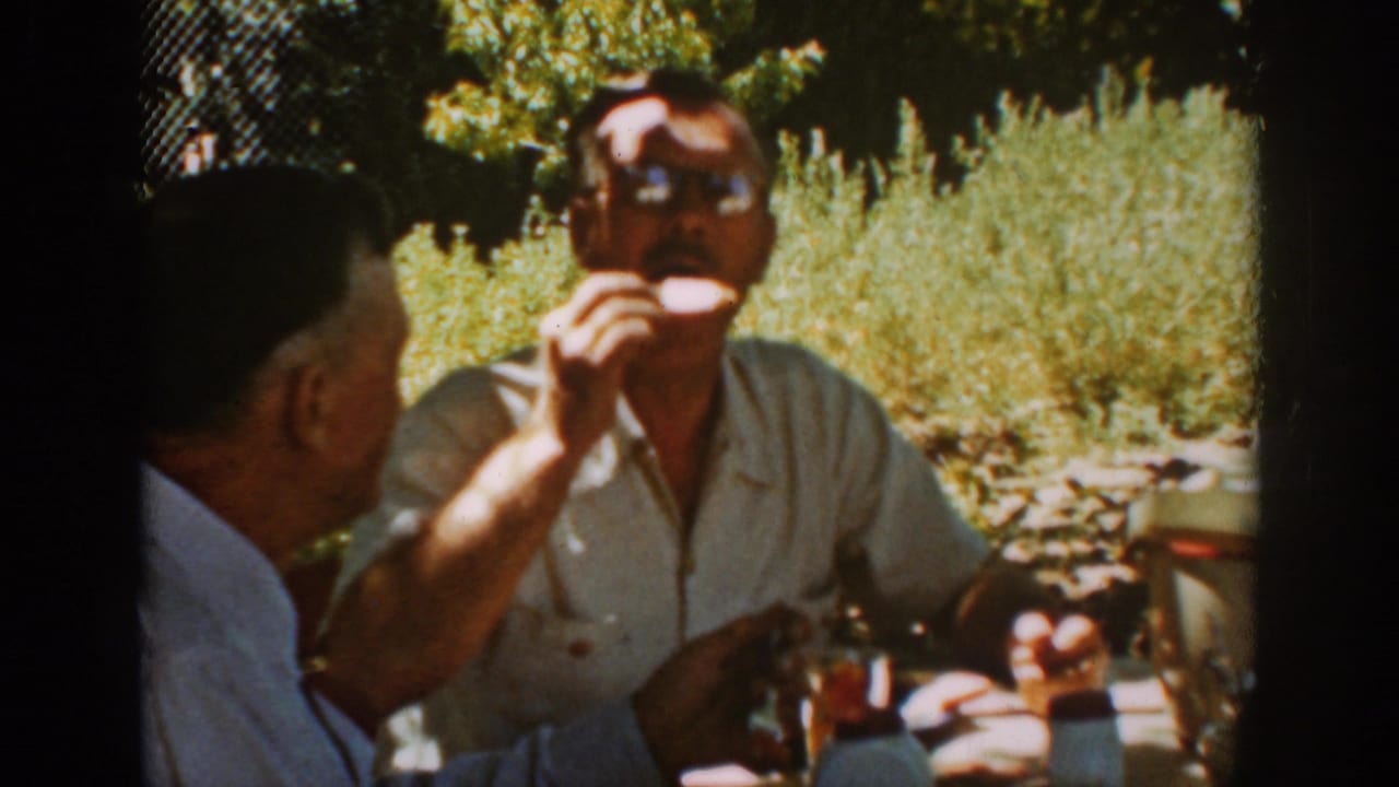 Man in sunglasses raises a drink at an outdoor table.