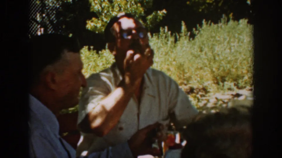 Close 1939 Auburn picnic view with one man drinking from a glass and another seated beside him at the outdoor table.