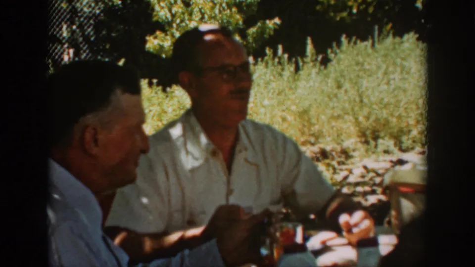 The Auburn home-movie frame shows a man in a light shirt speaking beside another older man in profile.