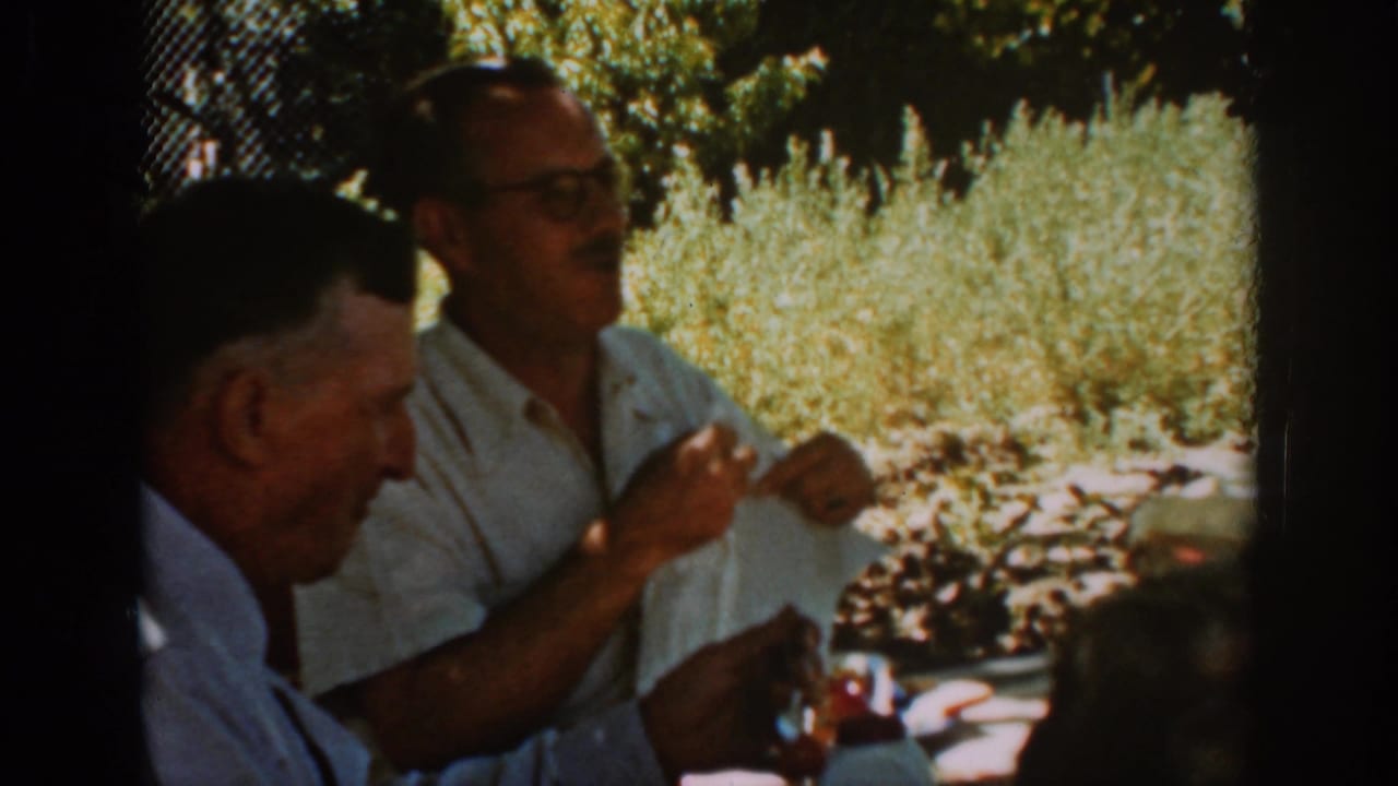 Man in a white shirt gestures while another man listens beside him.