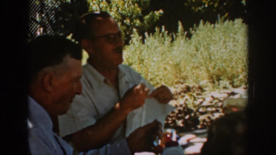 A 1939 Auburn outdoor meal scene shows a man in glasses gesturing with his hands while another seated man listens.