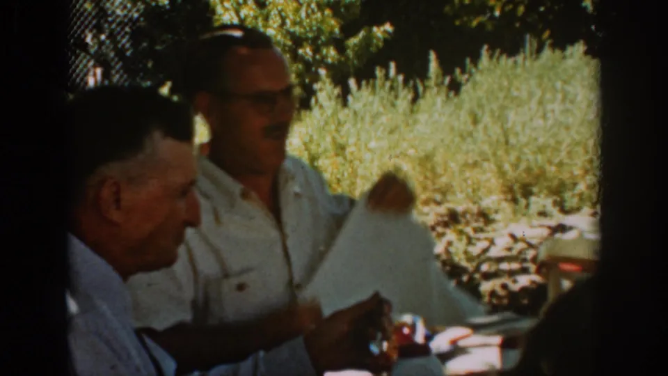 At the Auburn meal table, the man in a white shirt holds a light napkin or cloth as the other man sits nearby.