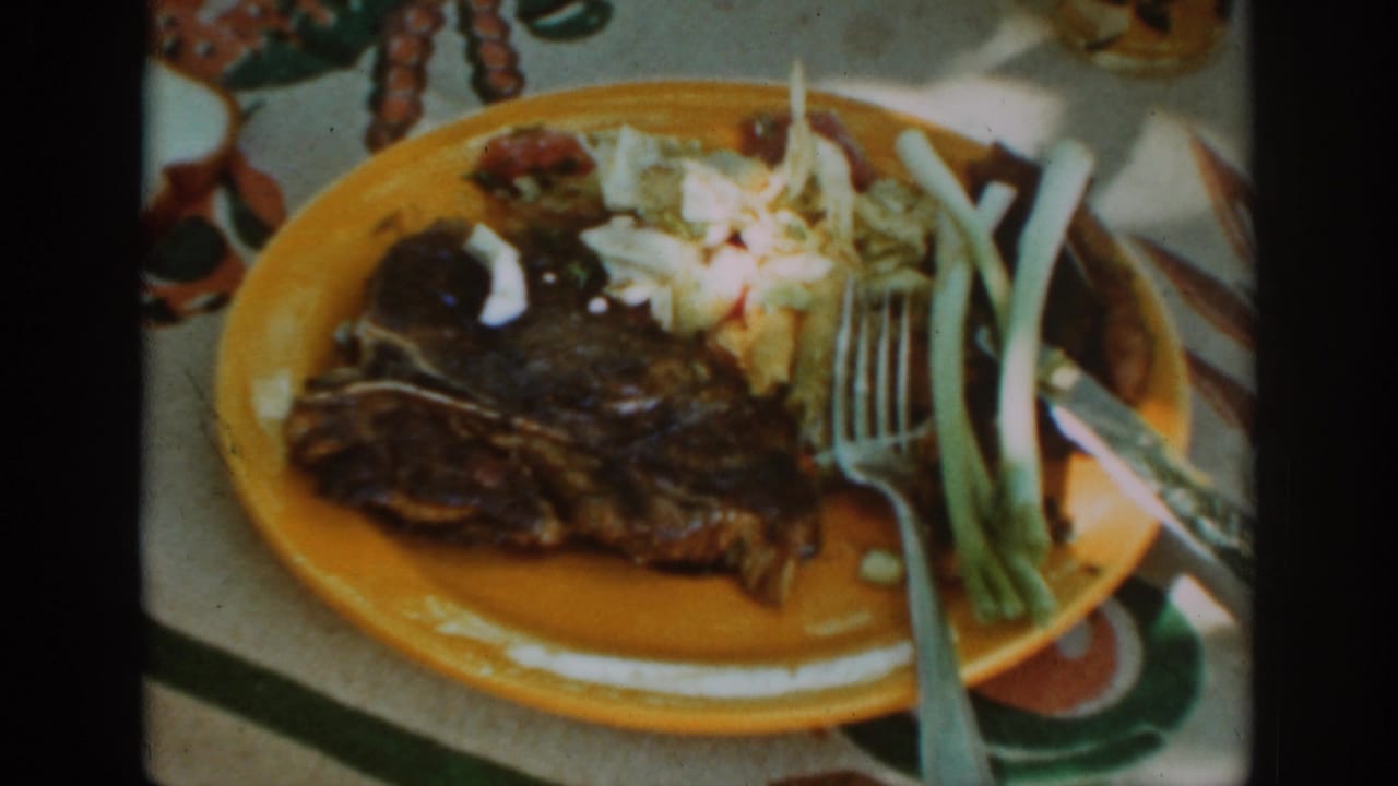 Similar close view of steak, coleslaw, green onions, fork, and knife on a yellow plate.