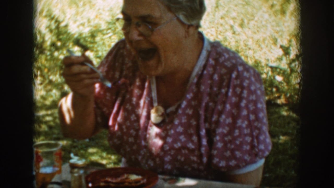 Older woman laughs while holding a spoon at an outdoor picnic table.