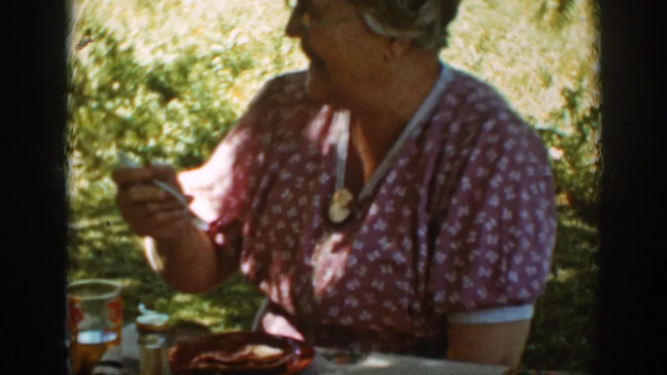 Near the end of the clip, the older woman turns toward someone off camera while seated at the Auburn picnic table.
