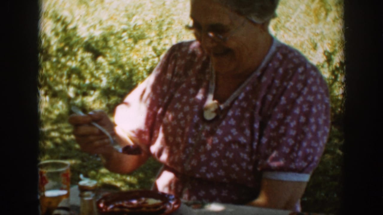Older woman in glasses seated outdoors with a fork near a plate.