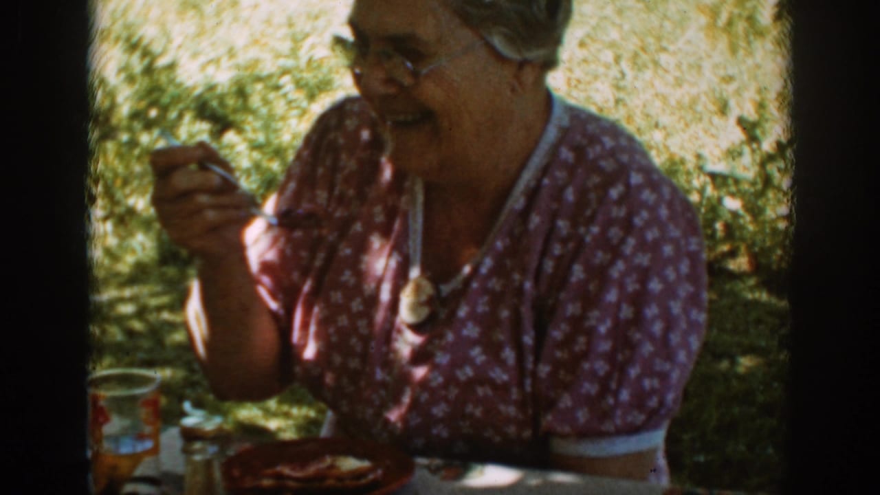 Smiling older woman in a floral dress holds a fork during an outdoor meal in Auburn, California, 1939.