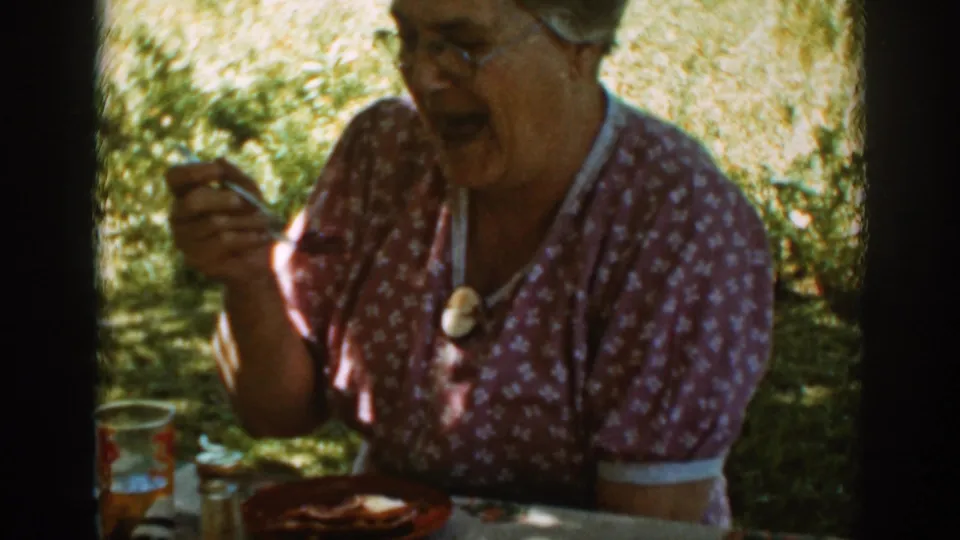 Older woman in glasses raises a fork toward her mouth during a shaded outdoor lunch in Auburn, California, 1939.