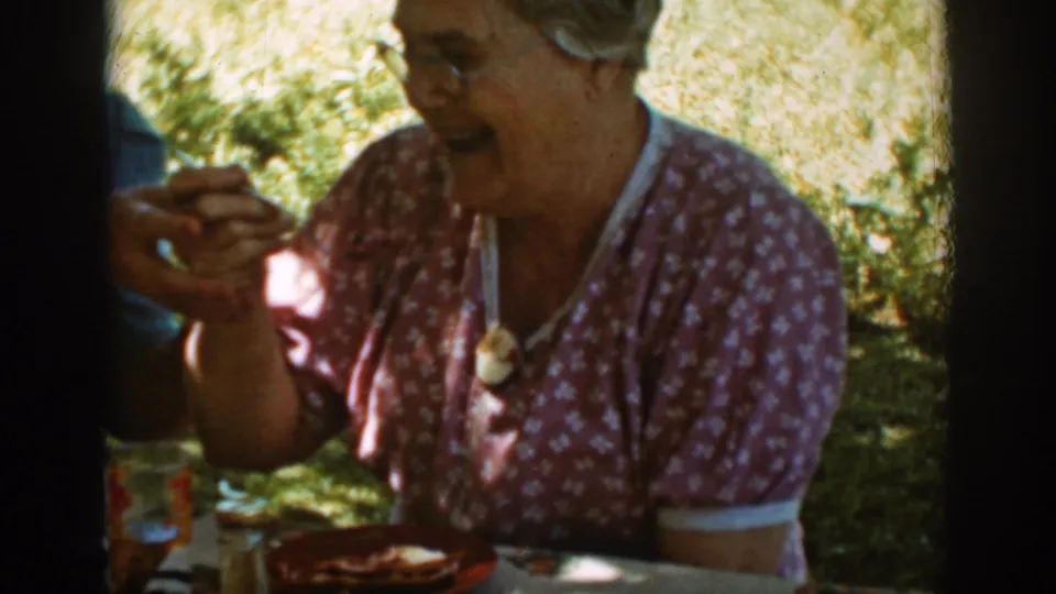 In supported 1939 Auburn, California home-movie footage, an older woman laughs at a shaded picnic table while holding food.