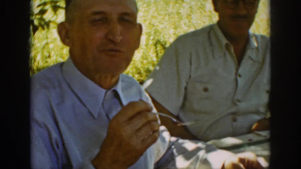 Auburn, California, 1939 home-movie frame showing a man chewing at an outdoor meal with a companion behind him.