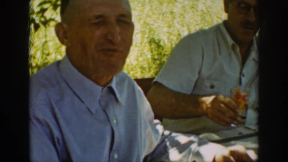 Auburn, California, 1939 frame of two adult men seated outside during a meal, with the foreground man facing the camera.