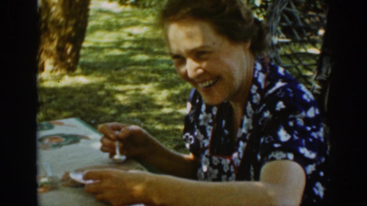 Older woman in a blue floral dress smiling at an outdoor table.