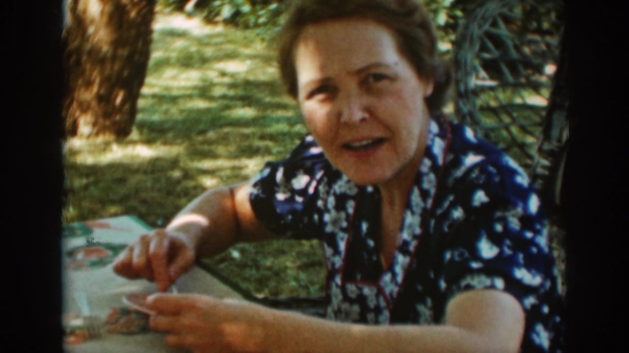 Older woman seated at a picnic table, holding a utensil near a plate outdoors.