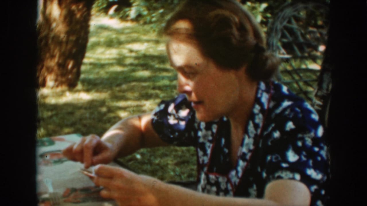 The woman turns to the side at the outdoor table, her face partly shadowed as she handles food with a utensil.