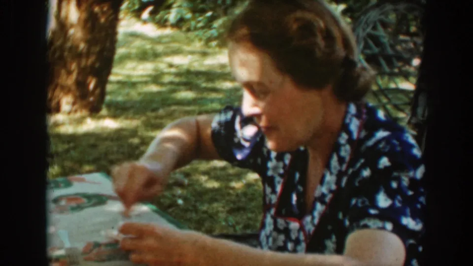 The woman looks down at the picnic table while scraping or moving food on a plate in the shaded Auburn lawn setting.